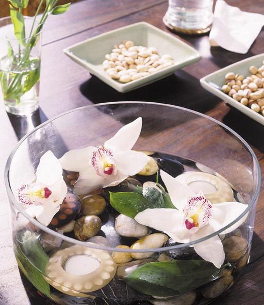 Flowers and pebbles inside a glass bow placed as a table centerpiece