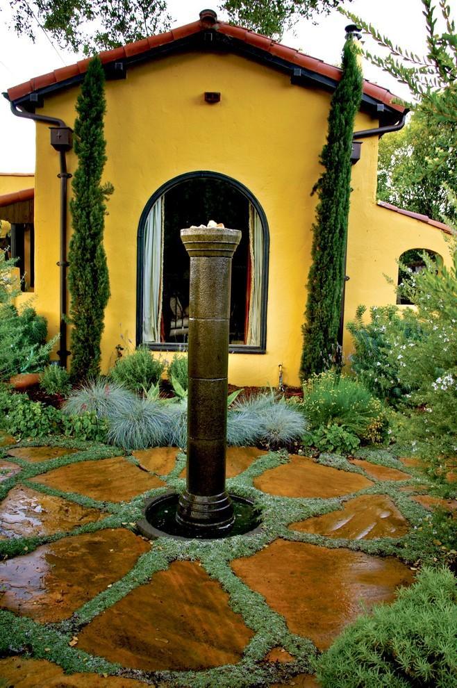 Mediterranean fountain in a garden with decorative flowers and yellow house facade