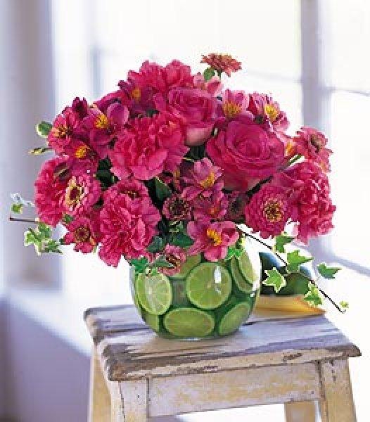 Red flowers inside a glass vessel full of citruses