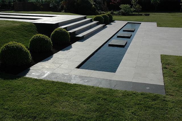 Minimalist garden with concrete tiles leading to an elegant swimming pool