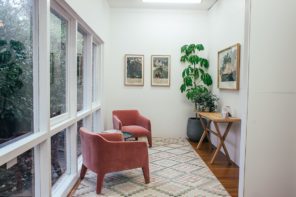 Interior of light hall with windows and armchairs on carpet near table and potted plant with pictures placed on white wall